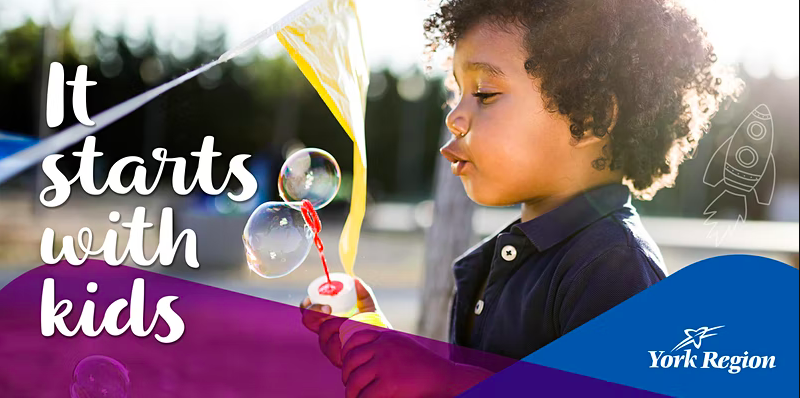 On the image, there is a child holding a bubble wand with their hand and blowing bubbles, along with a drawing of a rocket ship on  right. At the bottom there is blue and purple with the bottom left saying, York Region with their logo. On the left of the poster there is text saying "It starts with kids" 